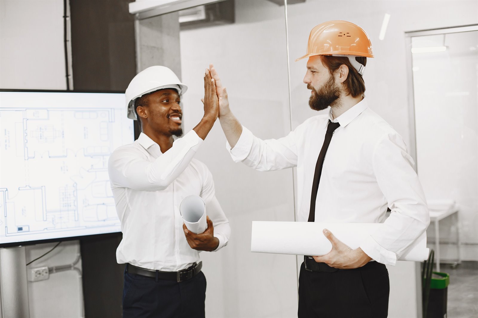 Deux ingénieurs en casque célèbrent leur collaboration devant des plans